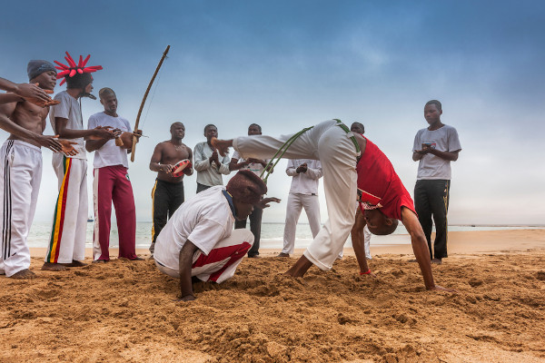 Dois homens lutando capoeira Angola em uma roda de capoeira na praia.