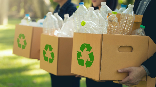 Três pessoas carregando caixas com materiais para reciclagem.